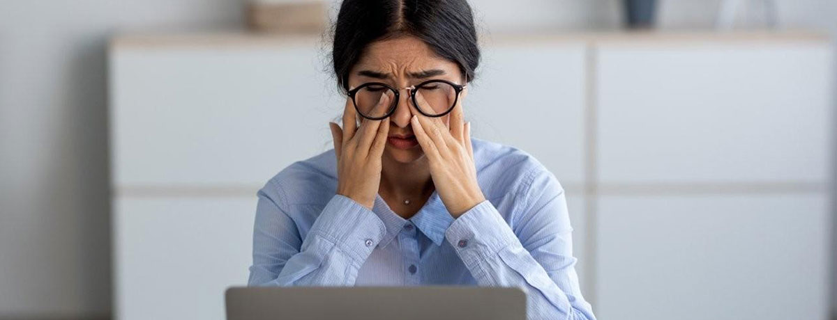 Woman with glasses rubbing at her eyes while looking at a laptop